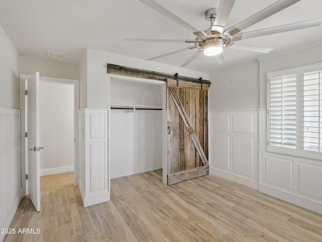 12210 N 67th St, Scottsdale, AZ 85254 - unfurnished bedroom with light wood-style floors, a closet, a barn door, a ceiling fan, and wainscoting