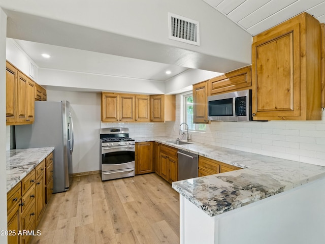 12210 N 67th St, Scottsdale, AZ 85254 - kitchen featuring appliances with stainless steel finishes, light wood finished floors, brown cabinets, light stone countertops, and a peninsula