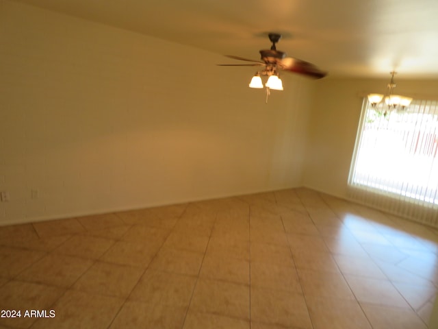 tiled spare room featuring ceiling fan with notable chandelier