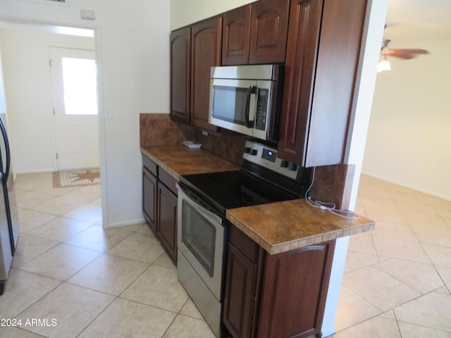 kitchen featuring ceiling fan, kitchen peninsula, appliances with stainless steel finishes, dark brown cabinets, and light tile patterned floors