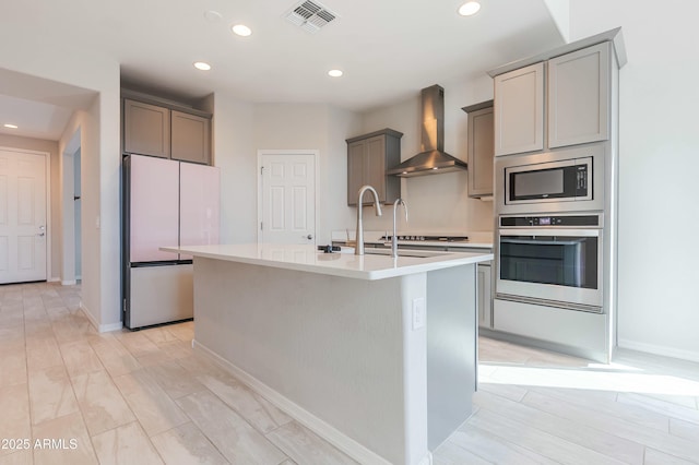 kitchen featuring visible vents, gray cabinetry, a kitchen island with sink, stainless steel appliances, and wall chimney range hood