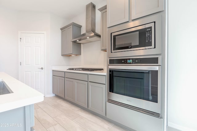 kitchen with light countertops, wall chimney exhaust hood, gray cabinets, and appliances with stainless steel finishes