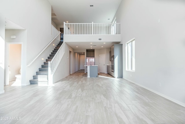 unfurnished living room with stairs, light wood-style flooring, baseboards, and a towering ceiling