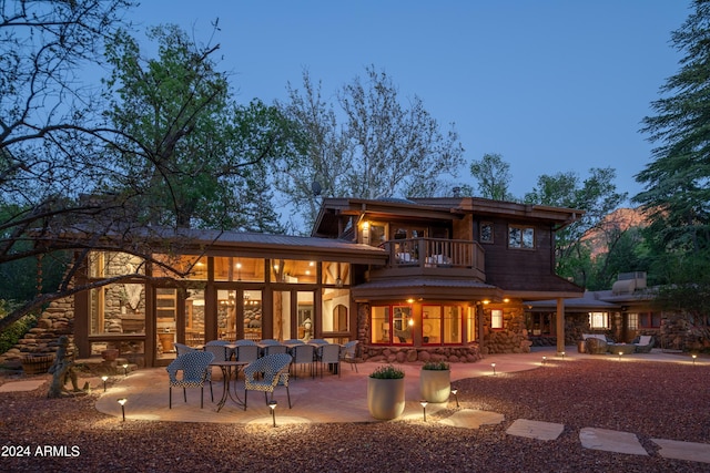 back house at dusk featuring a balcony and a patio area