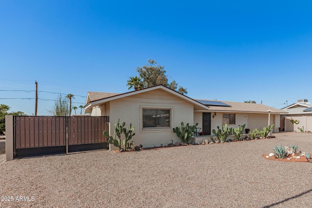 ranch-style house featuring roof mounted solar panels, fence, and a gate