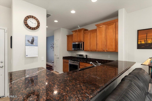 kitchen with kitchen peninsula, stainless steel appliances, dark stone counters, and a breakfast bar area