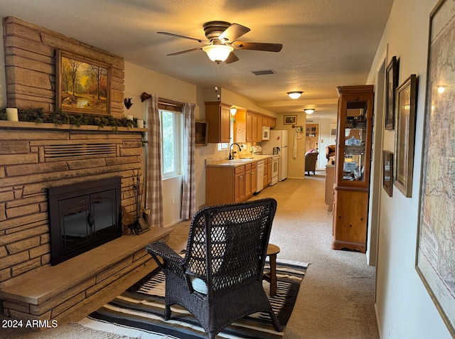 living room with sink, ceiling fan, a fireplace, a textured ceiling, and light colored carpet