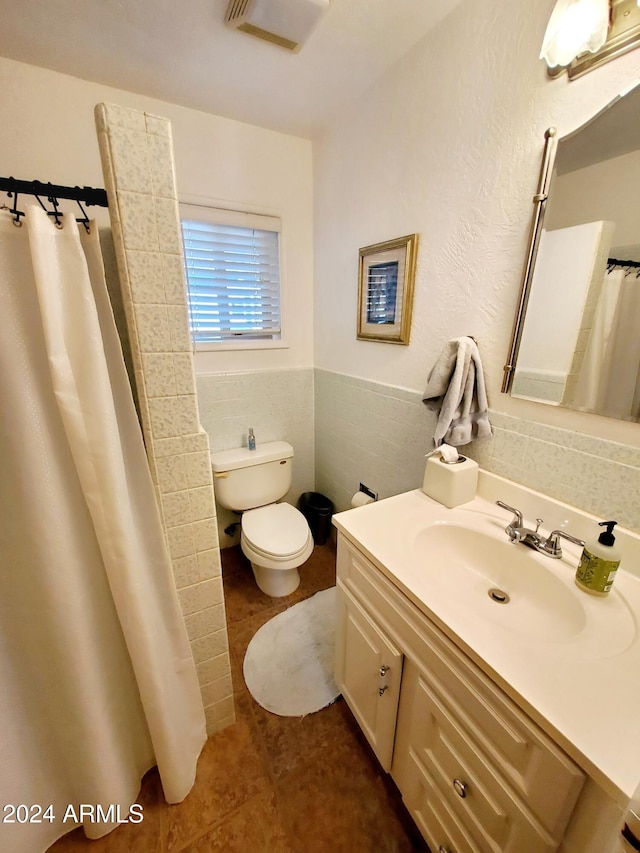 bathroom with tile patterned floors, vanity, tile walls, toilet, and curtained shower