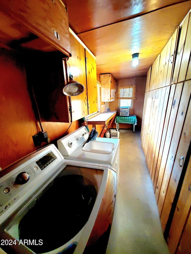 laundry room featuring washer and clothes dryer, wood walls, and cabinets