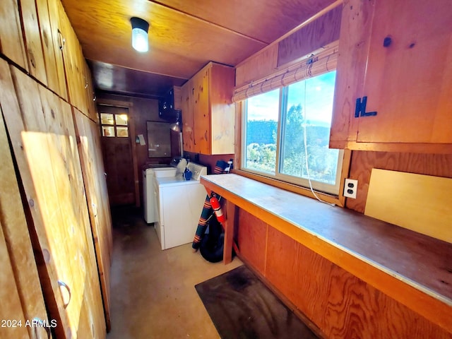 kitchen featuring wooden walls, washer and clothes dryer, and concrete flooring