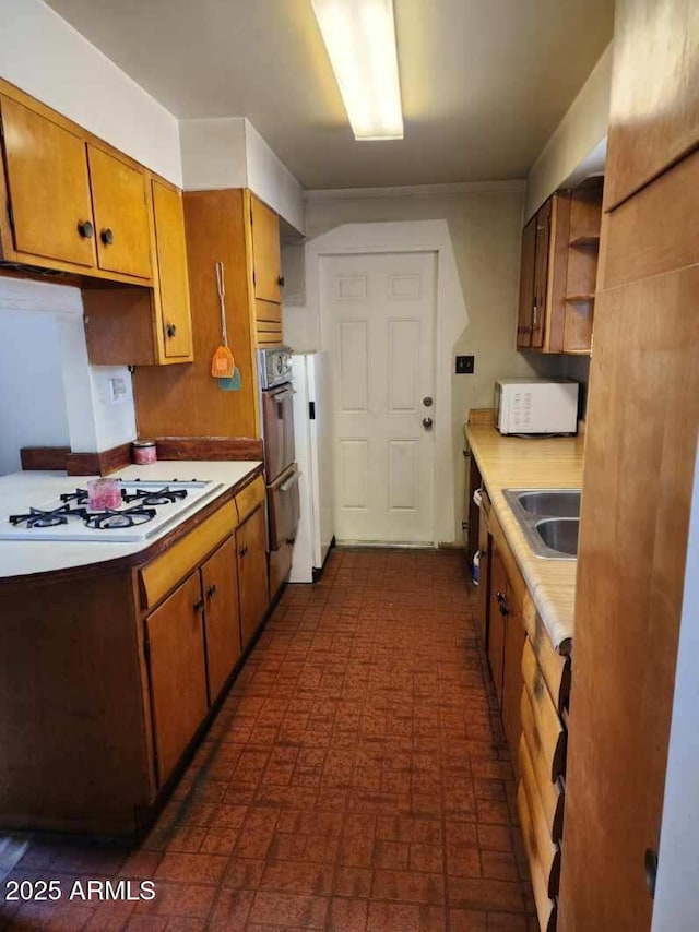 kitchen featuring white appliances, brown cabinetry, light countertops, open shelves, and a sink