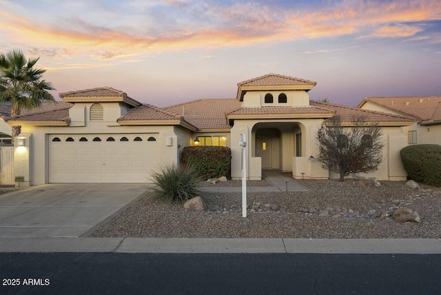 mediterranean / spanish house featuring driveway, a tiled roof, an attached garage, and stucco siding