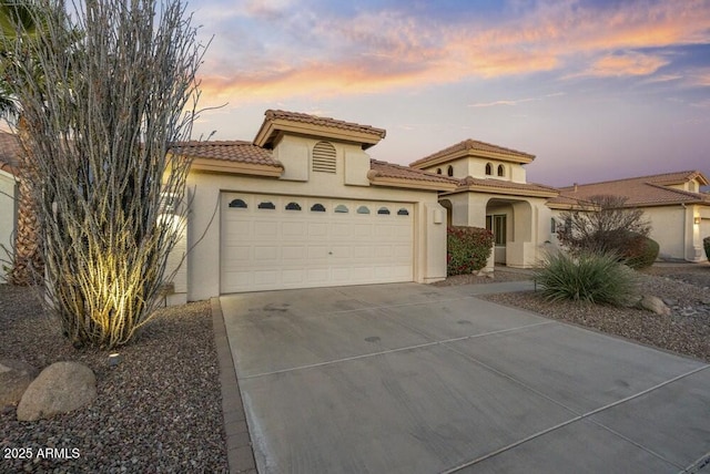 mediterranean / spanish-style home featuring a garage, driveway, a tiled roof, and stucco siding