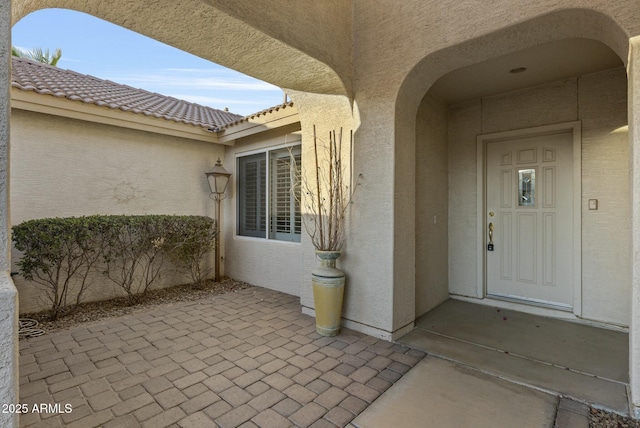 view of exterior entry with a patio area, a tile roof, and stucco siding