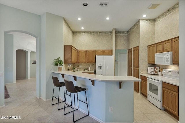 kitchen featuring light tile patterned floors, white appliances, a breakfast bar, tasteful backsplash, and kitchen peninsula