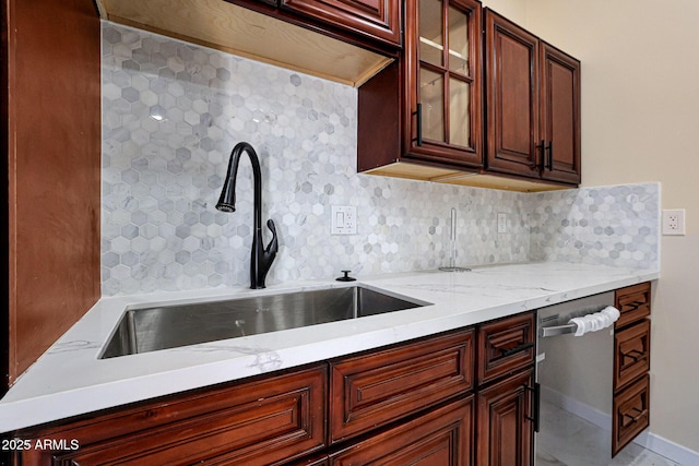 kitchen with stainless steel dishwasher, glass insert cabinets, light stone countertops, a sink, and backsplash