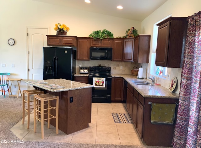 kitchen featuring a kitchen bar, black appliances, a sink, a kitchen island, and light tile patterned flooring