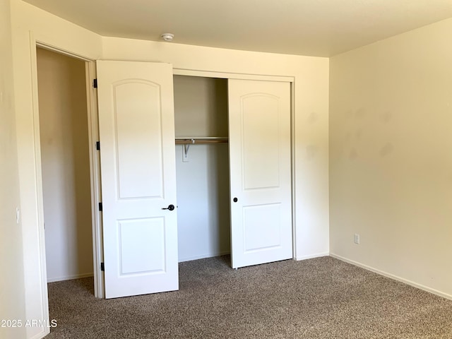 unfurnished bedroom featuring a closet, dark carpet, and baseboards