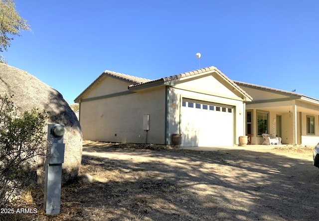 view of side of home with stucco siding, a tiled roof, driveway, and a garage