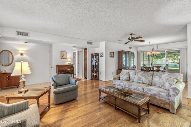 living room featuring ceiling fan with notable chandelier, light hardwood / wood-style floors, and a textured ceiling