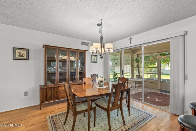 dining room with a textured ceiling, an inviting chandelier, and light hardwood / wood-style flooring