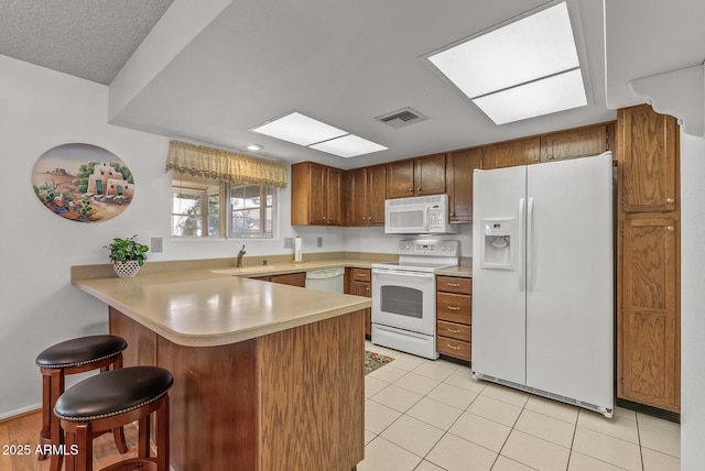 kitchen featuring white appliances, sink, kitchen peninsula, light tile patterned flooring, and a breakfast bar area