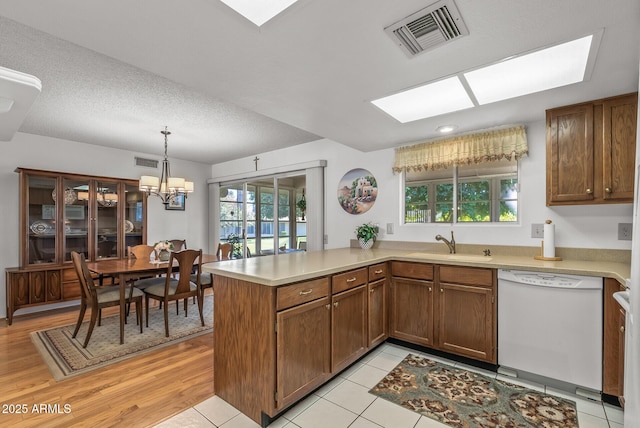 kitchen with decorative light fixtures, kitchen peninsula, sink, white dishwasher, and a chandelier