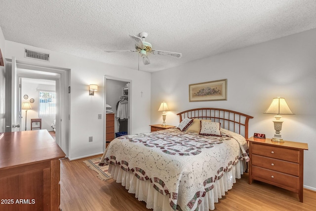 bedroom with light wood-type flooring, a closet, a walk in closet, and ceiling fan