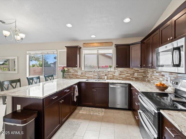 kitchen featuring light stone counters, a sink, stainless steel appliances, a peninsula, and tasteful backsplash