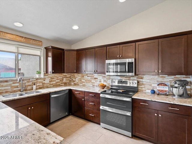 kitchen featuring lofted ceiling, dark brown cabinets, a sink, appliances with stainless steel finishes, and backsplash