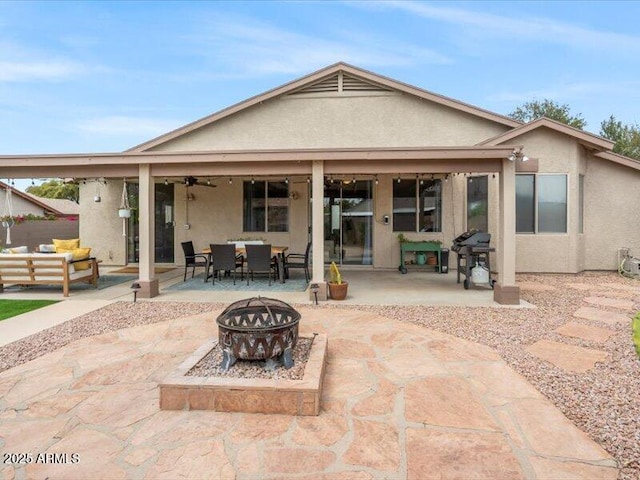 rear view of house with a ceiling fan, outdoor dining area, a patio area, a fire pit, and stucco siding