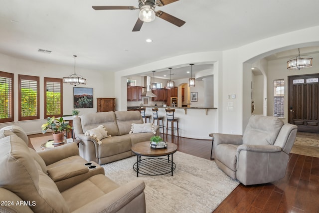 living room with ceiling fan with notable chandelier and dark hardwood / wood-style flooring