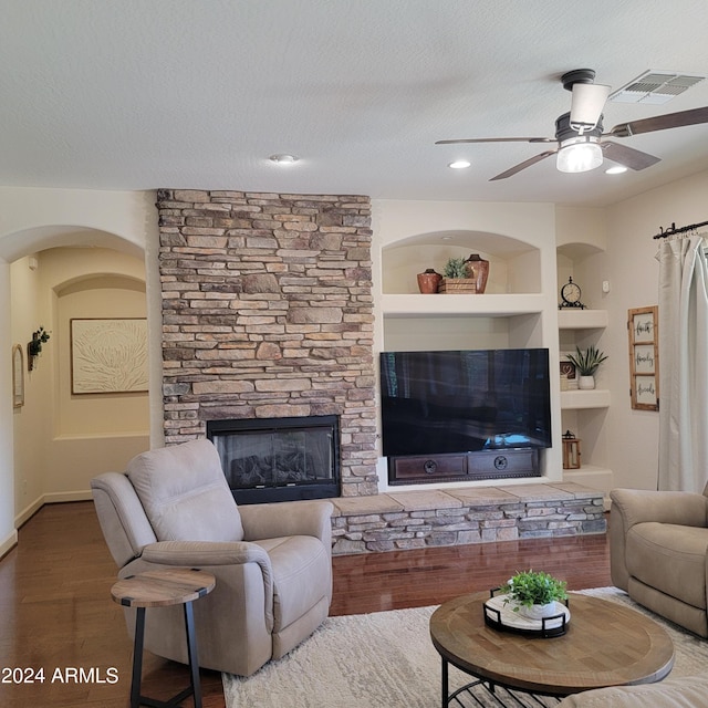 living room with built in shelves, a textured ceiling, hardwood / wood-style floors, and a stone fireplace