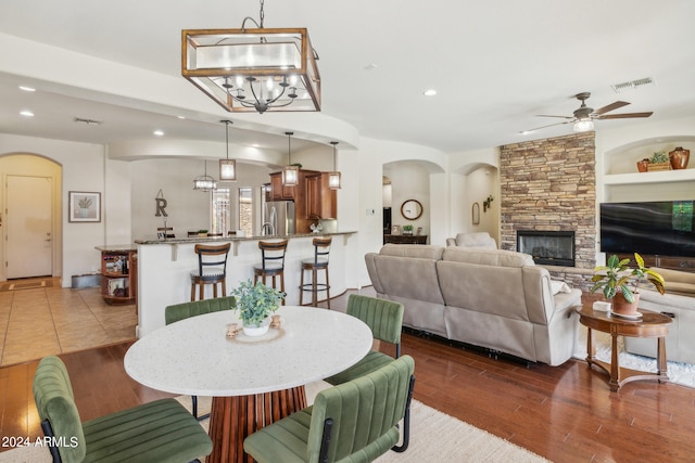 dining area featuring built in shelves, a stone fireplace, ceiling fan with notable chandelier, and dark wood-type flooring