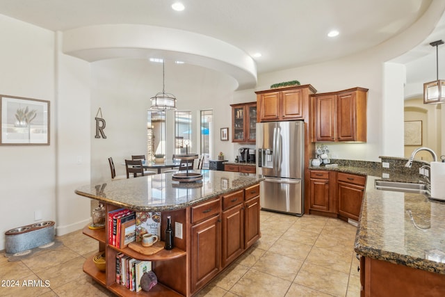 kitchen featuring hanging light fixtures, sink, a kitchen island, stainless steel fridge with ice dispenser, and dark stone counters