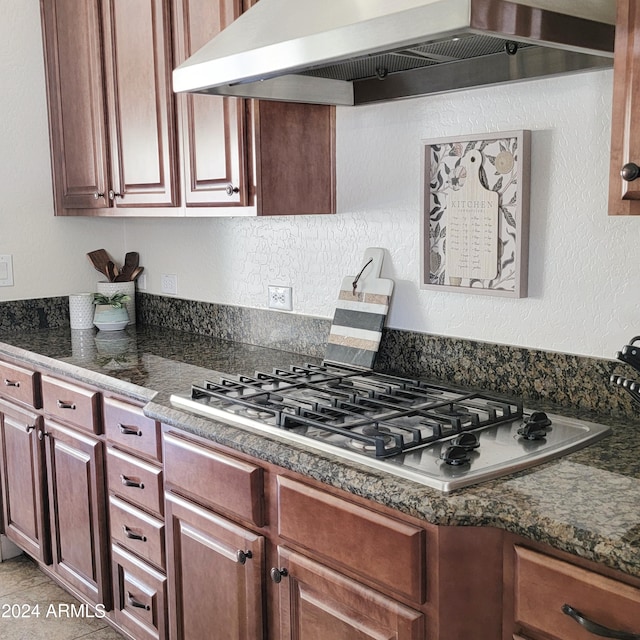 kitchen with dark stone countertops, stainless steel gas cooktop, and wall chimney range hood