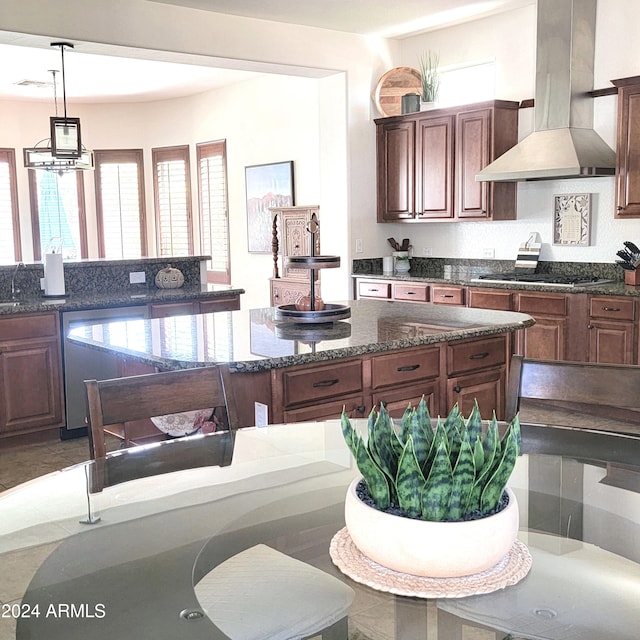 kitchen with wall chimney range hood, an inviting chandelier, stainless steel appliances, decorative light fixtures, and dark stone countertops