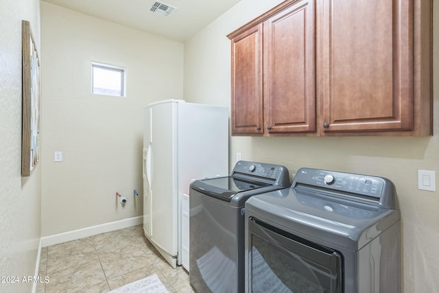 clothes washing area featuring light tile patterned floors, washing machine and clothes dryer, and cabinets