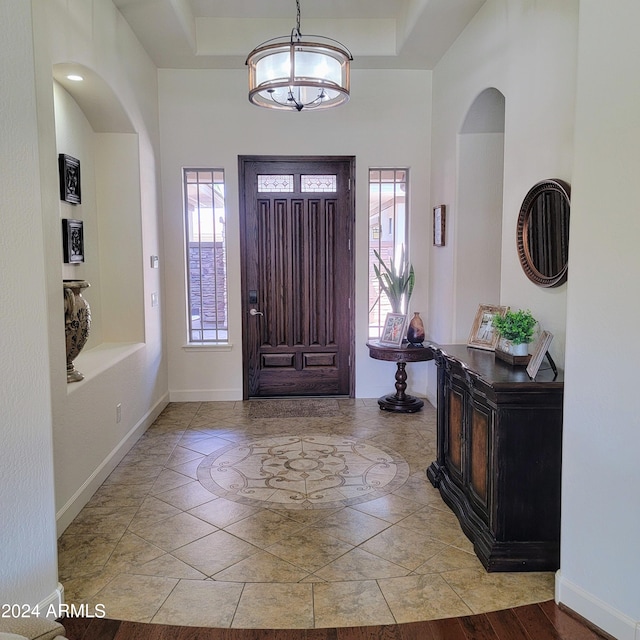 foyer entrance with a healthy amount of sunlight, a raised ceiling, and a notable chandelier