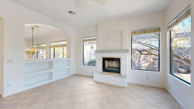 unfurnished living room with an inviting chandelier, light tile patterned floors, and built in features