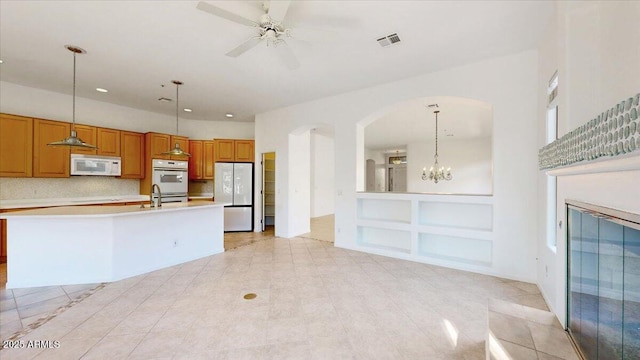 kitchen with ceiling fan with notable chandelier, pendant lighting, an island with sink, sink, and white appliances