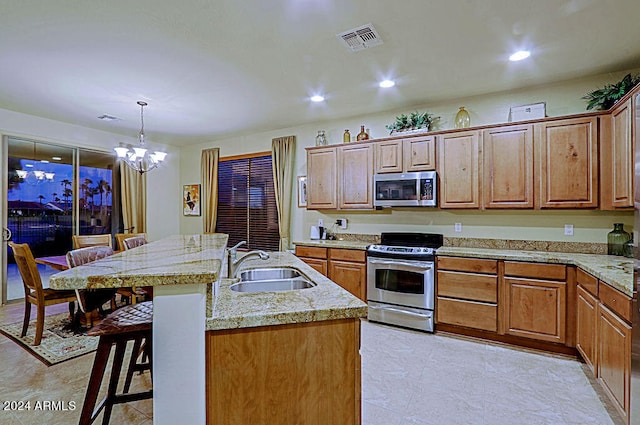 kitchen with an island with sink, appliances with stainless steel finishes, a breakfast bar, sink, and decorative light fixtures