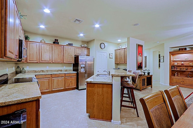 kitchen featuring a breakfast bar area, an island with sink, stainless steel appliances, sink, and light stone countertops