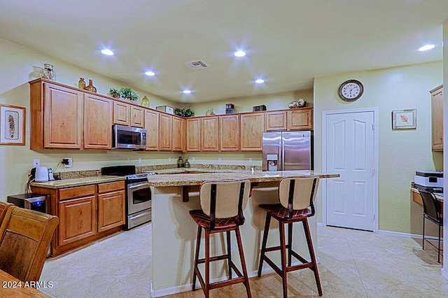 kitchen featuring a kitchen island, appliances with stainless steel finishes, light stone counters, and a breakfast bar