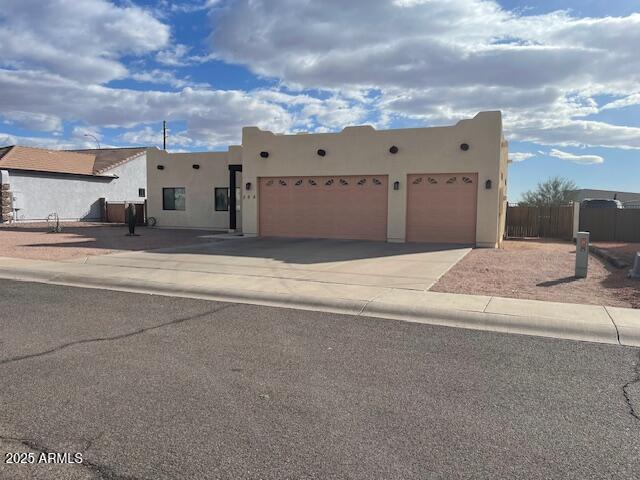 pueblo revival-style home with stucco siding, concrete driveway, an attached garage, and fence