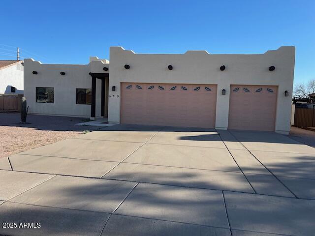 pueblo-style house with stucco siding, a garage, concrete driveway, and fence