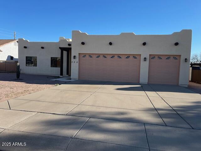 pueblo-style home with an attached garage, fence, driveway, and stucco siding