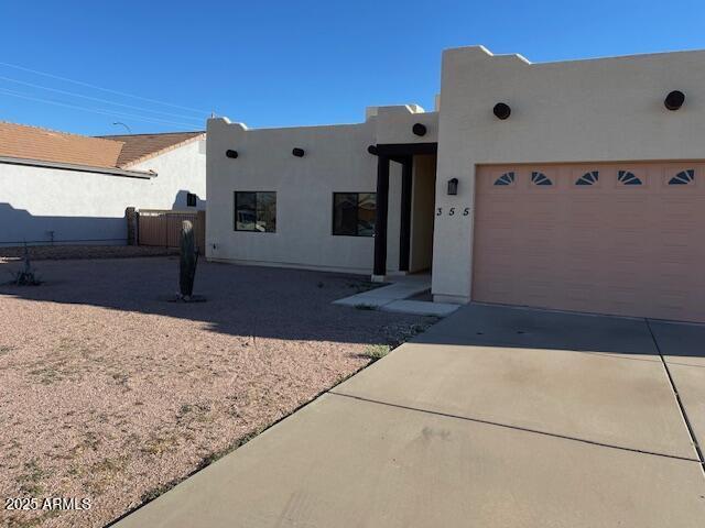 pueblo revival-style home featuring stucco siding, a garage, and concrete driveway