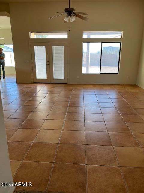 tiled spare room featuring french doors, a ceiling fan, and a towering ceiling