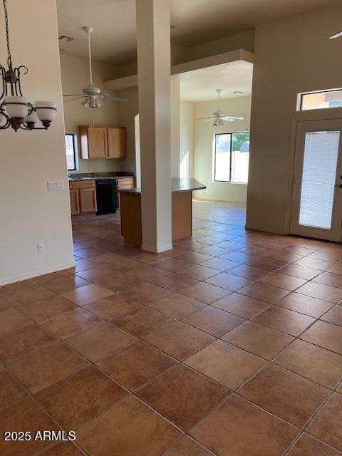 interior space featuring dark tile patterned floors, ceiling fan with notable chandelier, dark countertops, a high ceiling, and dishwasher